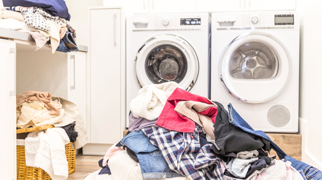 Clothes pile beside a washing machine.